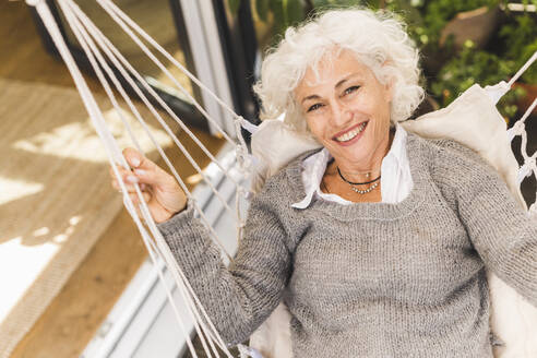 Smiling mature woman sitting on swing at home - UUF21631