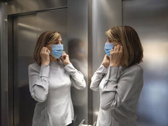 Senior woman wearing protective face mask while standing in elevator during covid-19 - ZEDF03829