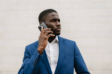 Young businessman looking away while on the phone against wall in city - EGAF00832