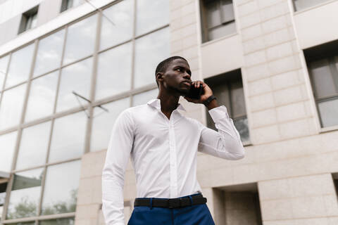 Male professional on the phone looking away while standing against office building in city stock photo