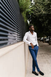 Junger männlicher Unternehmer, der wegschaut, während er sich an eine Mauer in der Stadt lehnt - EGAF00839