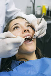 Dentist in gloves examining oral cavity of pretty patient at clinic - ABZF03355