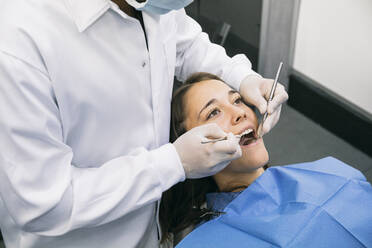 Male dentist inspecting oral cavity of young female patient at clinic - ABZF03359