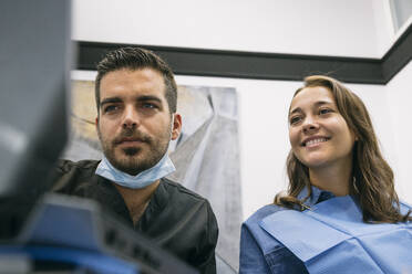 Schöne Patientin freut sich über die Erklärungen eines gutaussehenden männlichen Zahnarztes am Laptop in der Klinik - ABZF03366