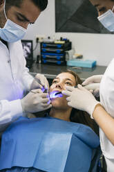 Männlicher Zahnarzt untersucht die Zähne einer Patientin mit Hilfe einer Assistentin in der Klinik - ABZF03371
