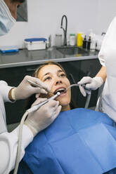 Male dentist doing dental treatment of female patient with help of assistant at clinic - ABZF03372