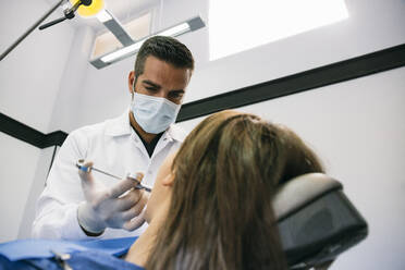 Male dentist anesthetizing female patient before dental treatment at clinic - ABZF03384