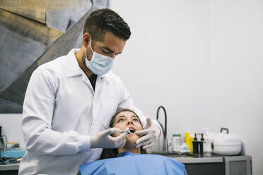 Male dentist anesthetizing young female patient before dental treatment at clinic - ABZF03385