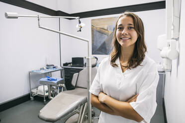Lächelnde junge Zahnarzthelferin steht mit verschränkten Armen in einer Klinik - ABZF03395