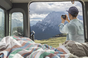 Mann fotografiert eine malerische Bergkette, während er neben einem Wohnmobil steht. Sextner Dolomiten, Dolomiten, Südtirol, Italien - MMAF01403