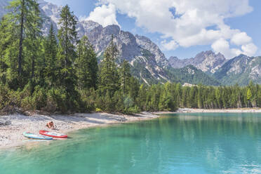 Mann mit Paddelbrett am Ufer des Pragser Wildsees an einem sonnigen Tag, Dolomiten, Südtirol, Italien - MMAF01423