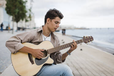 Junger Mann spielt Gitarre beim Üben an der Promenade gegen den Himmel - DCRF00877
