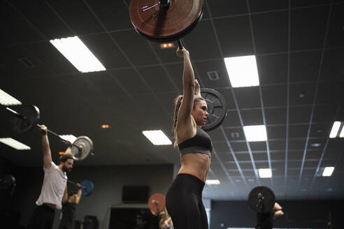 Frauen und Männer trainieren mit einer Langhantel im Stehen in einem Fitnessstudio - SNF00552