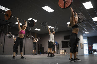 Athletes lifting barbell while exercising in gym - SNF00553