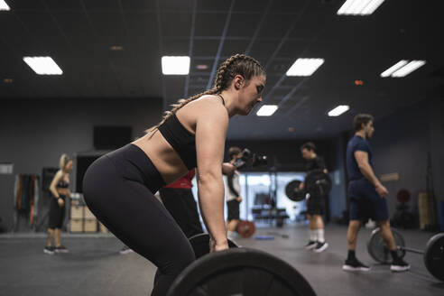 Woman picking barbell with people exercising in background at gym - SNF00557