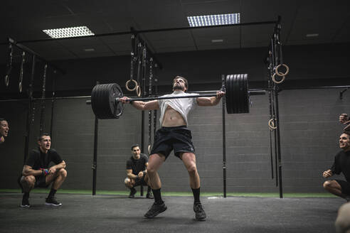 People cheering man lifting barbell while standing in gym - SNF00560