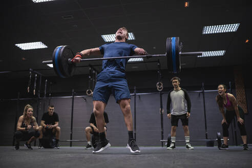 Adaptive athlete jumping while lifting barbell with people cheering in background at gym - SNF00561