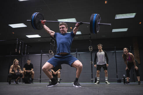 Athletes cheering man picking barbell while standing at gym - SNF00562