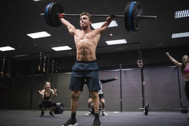 Amputee athlete picking barbell with people cheering in background at gym - SNF00563