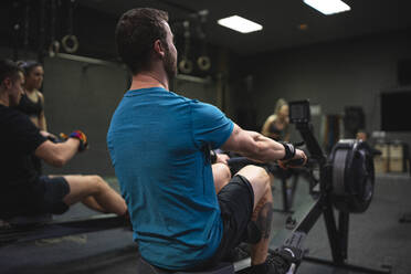 Man using rowing machine with people exercising in background at gym - SNF00567