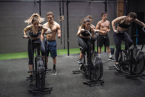 Men motivating women exercising on fitness bike at gym stock photo