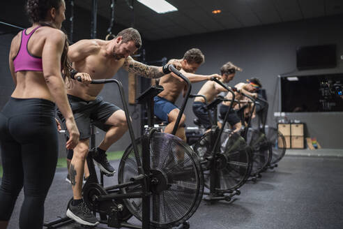 Athletes sitting on bike while exercising at gym - SNF00574