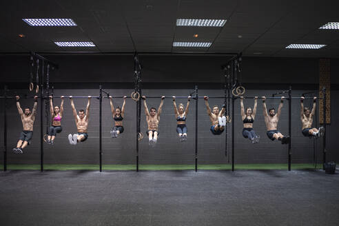 Male and female athletes hanging on rod at gym - SNF00583