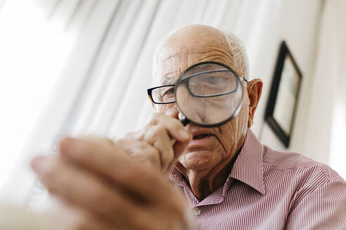 Ein älterer Mann im Ruhestand betrachtet ein Fossil durch ein Vergrößerungsglas - JRFF04763