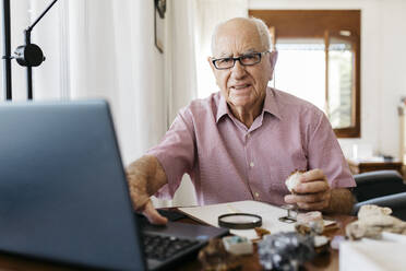 Älterer Mann im Ruhestand recherchiert Fossilien und Mineralien, während er zu Hause am Laptop sitzt - JRFF04767