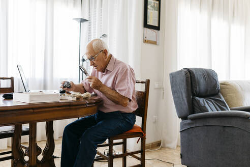 Älterer Mann im Ruhestand, der zu Hause ein Vergrößerungsglas zur Untersuchung von Fossilien und Mineralien benutzt - JRFF04771