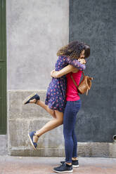 Lesbian couple embracing while standing against wall in city - JSMF01765