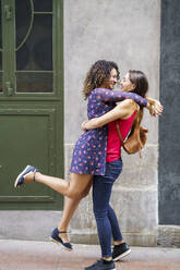 Women looking at each other while embracing against wall in city - JSMF01766