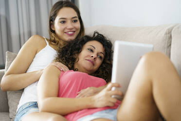 Beautiful lesbian couple using digital tablet while lying on sofa at home - JSMF01797