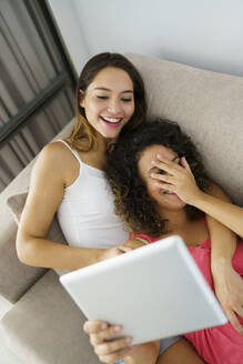 Weibliches Paar benutzt ein digitales Tablet, während es sich zu Hause auf dem Sofa ausruht - JSMF01798
