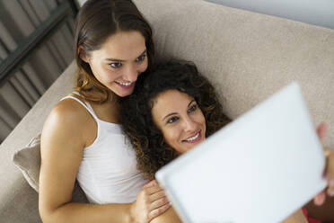 Lesbisches Paar benutzt digitales Tablet, während es sich zu Hause auf dem Sofa ausruht - JSMF01799