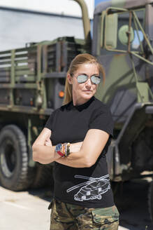 Confident mature female army soldier standing with arms crossed while looking away against truck on sunny day - MTBF00672