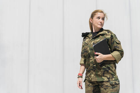 Ältere blonde weibliche Armee Soldat hält digitale Tablet, während der Blick weg auf Militärbasis an einem sonnigen Tag - MTBF00681