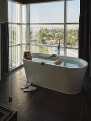 Frau nimmt ein Bad in der Badewanne vor dem Fenster eines Luxushotels - ZEDF03887