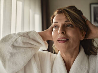 Close-up of smiling woman looking away with hands in blond hair at hotel room - ZEDF03904