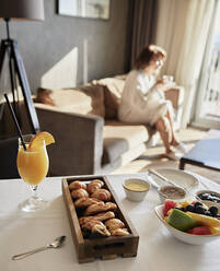Frisches Frühstück auf dem Tisch mit einer älteren Frau, die auf dem Sofa eines Luxushotels sitzt - ZEDF03909