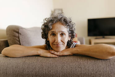 Mature woman resting on sofa at home - TCEF01195