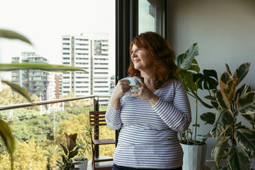 Lächelnde Frau beim Kaffeetrinken auf dem Balkon zu Hause - VABF03563