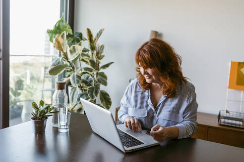 Reife Frau sitzt am Tisch und arbeitet zu Hause am Laptop - VABF03575