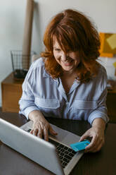 Lächelnde Frau beim Online-Shopping am Laptop, während sie zu Hause sitzt - VABF03576