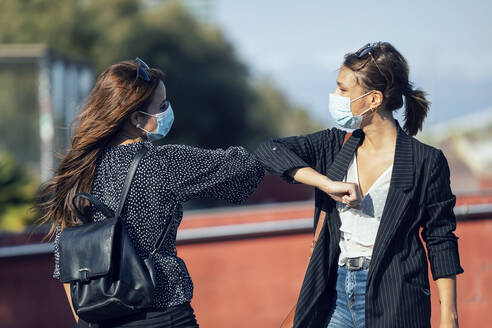 Friends wearing face mask giving elbow bumps while standing in city - JSRF01165