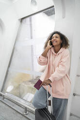 Lächelnde junge Frau, die am Flughafen steht und mit ihrem Smartphone spricht - SNF00592