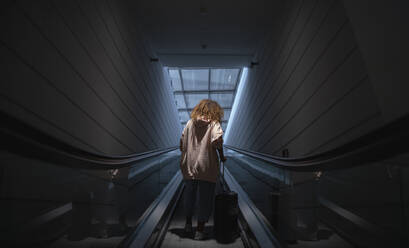 Young woman holding suitcase standing on escalator at airport - SNF00593