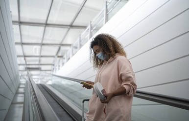 Junge Frau benutzt ihr Smartphone, während sie auf einer Rolltreppe im Flughafen steht - SNF00597