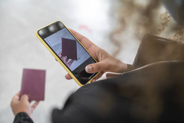 Frau fotografiert ihren Reisepass mit dem Smartphone, während sie am Flughafen steht - SNF00603