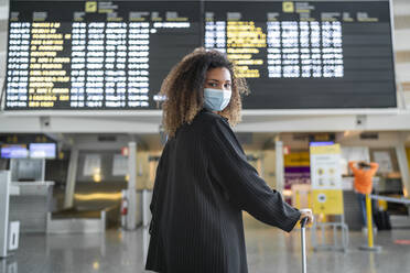 Woman wearing protective face mask looking over shoulder while standing at airport - SNF00604